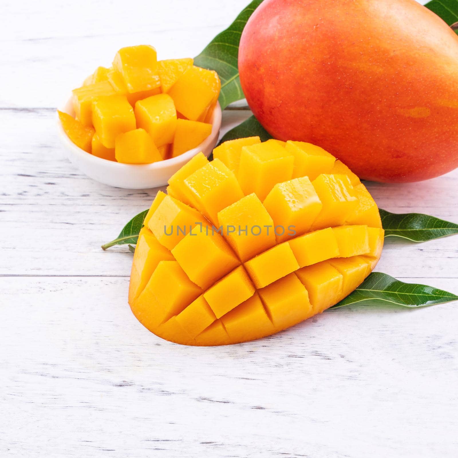 Fresh mango,beautiful chopped fruit with green leaves on bright wooden table background. Tropical fruit design concept, close up, copy space.