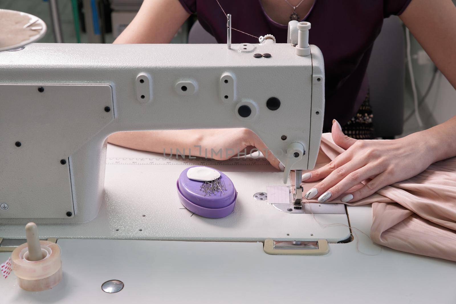 Woman using sewing machine in tailor studio or modern atelier shop
