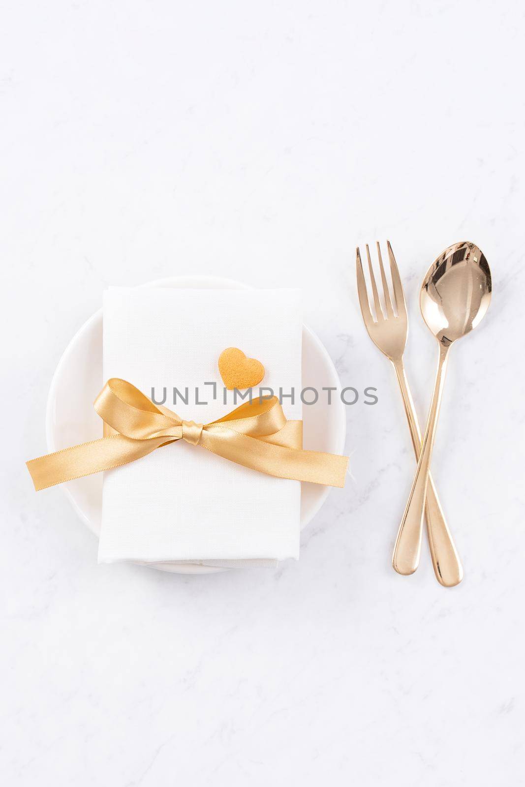 Valentine's Day, Mother's Day, holiday dating meal, banquet design concept - White plate and golden ribbon on marble background, top view, flat lay.
