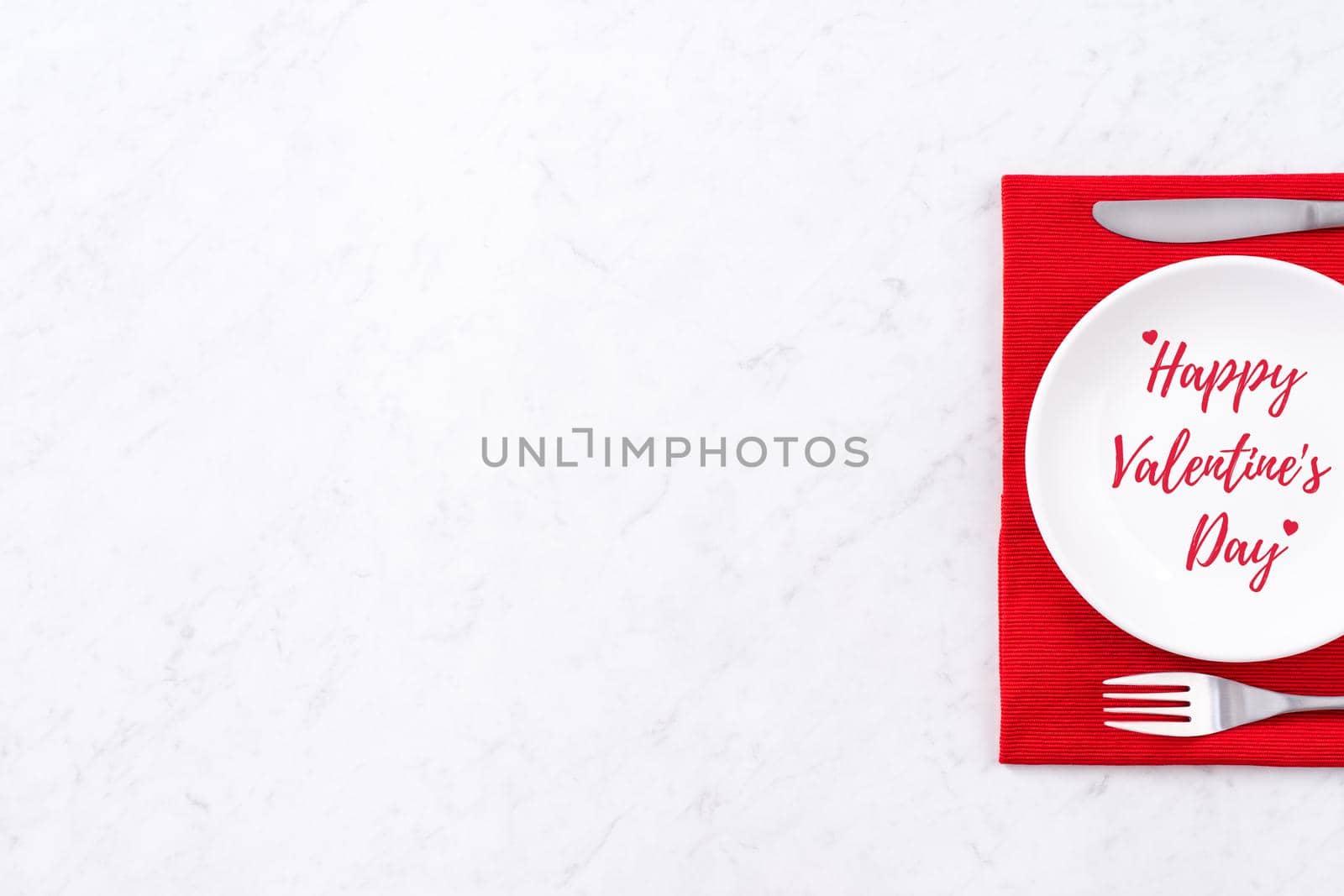 Valentine's Day holiday dating meal, banquet greeting card design concept - White plate and red ribbon on marble background, top view, flat lay.