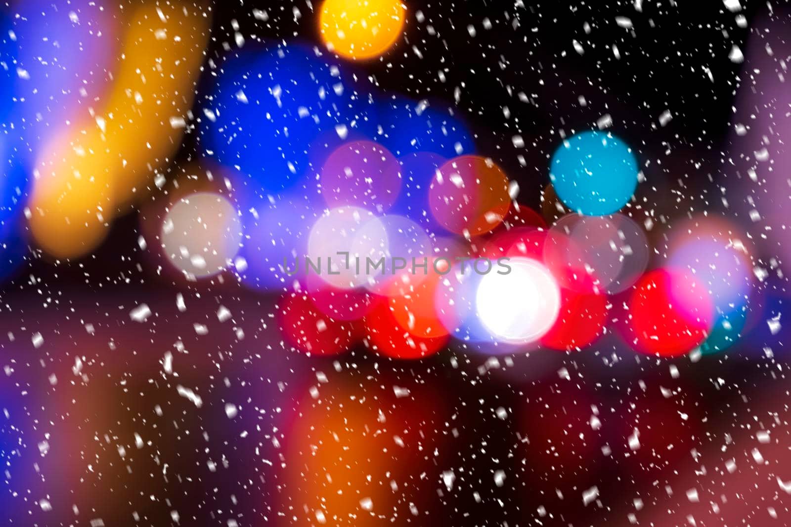 Blurred lights of headlights of cars and lanterns in the night city in a snowfall. Abstract bright bokeh.