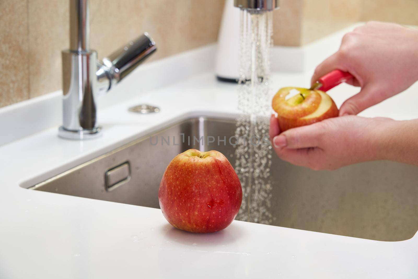Female Hands Cutting And Peeling Skin Off Of Red Apple Using Sharp Knife At Kitchen Sink