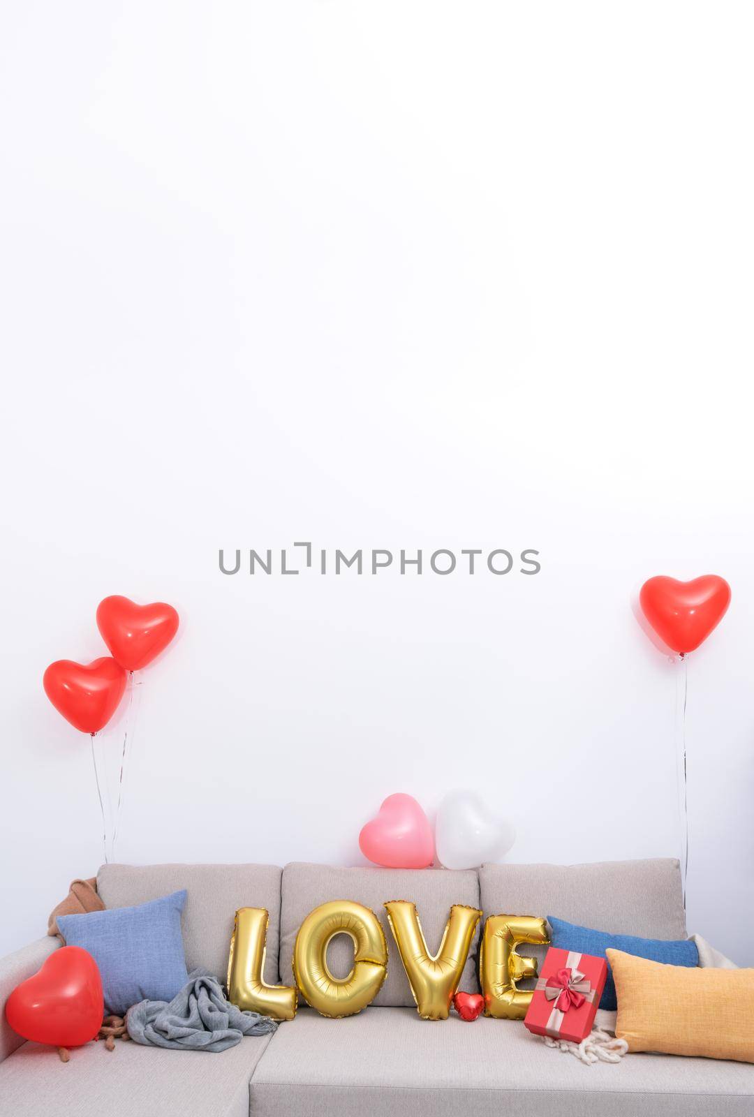 Foil love balloons and gifts on a sofa with white wall in background for Valentine's day, Mother's day surprise design concept.