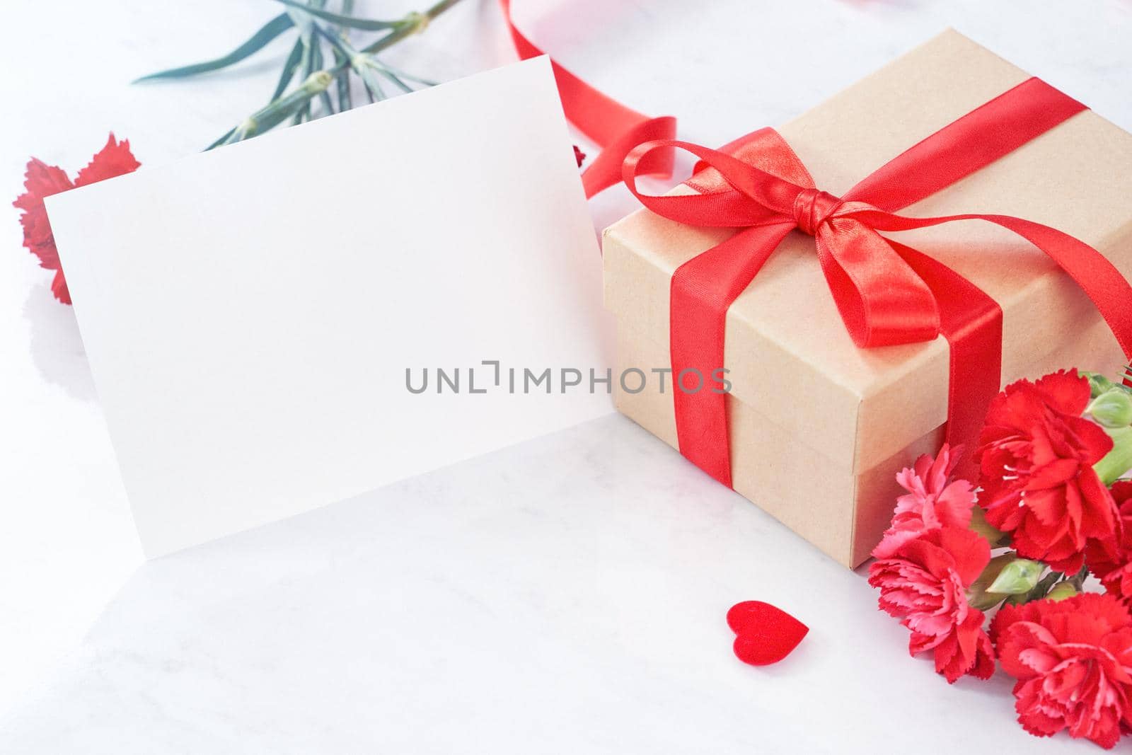 Mother's Day greeting design concept - Beautiful blooming red carnations, gift box with ribbon on white marble table background, close up, copy space.