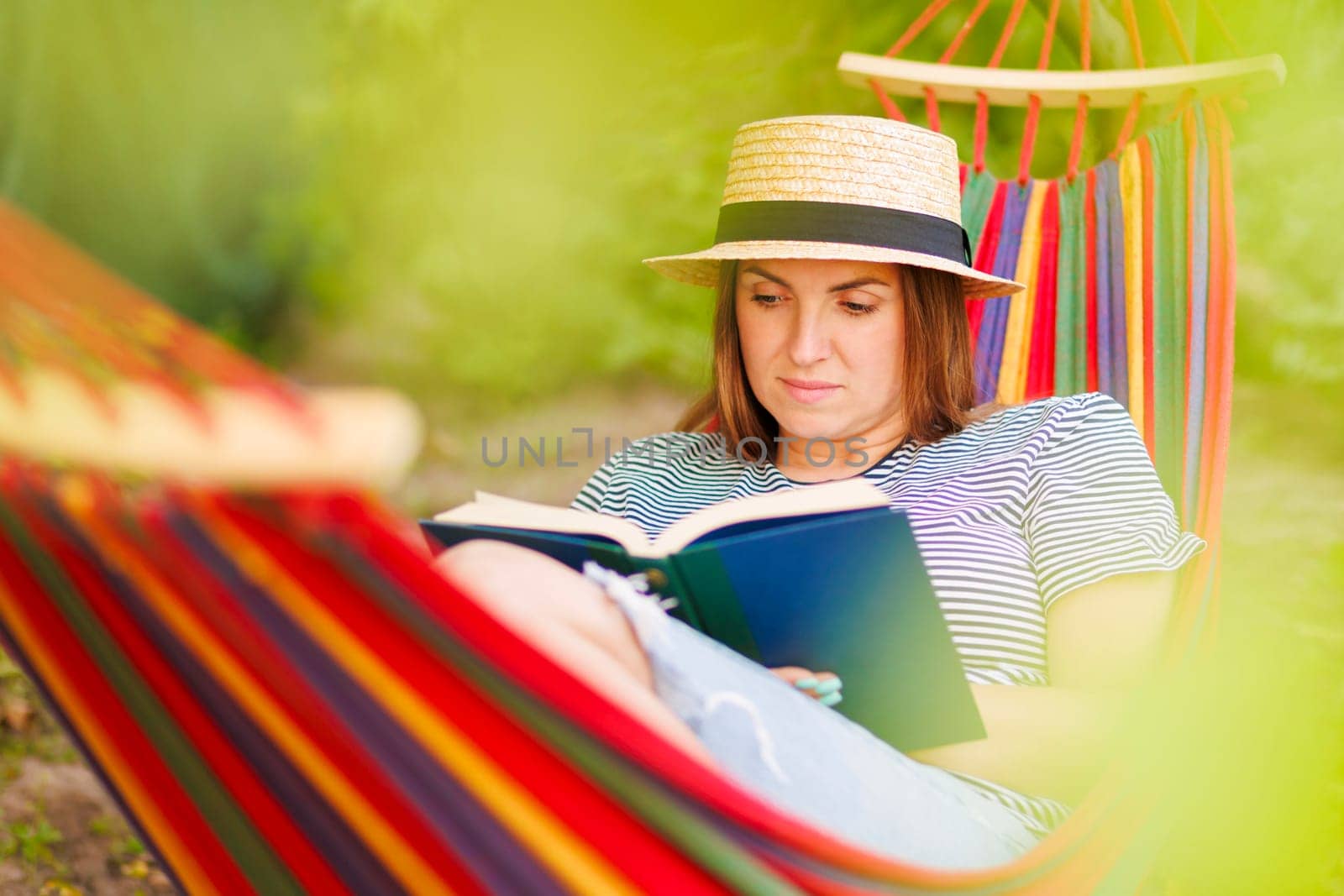 Young woman reading book while lying in comfortable hammock at green garden by andreyz