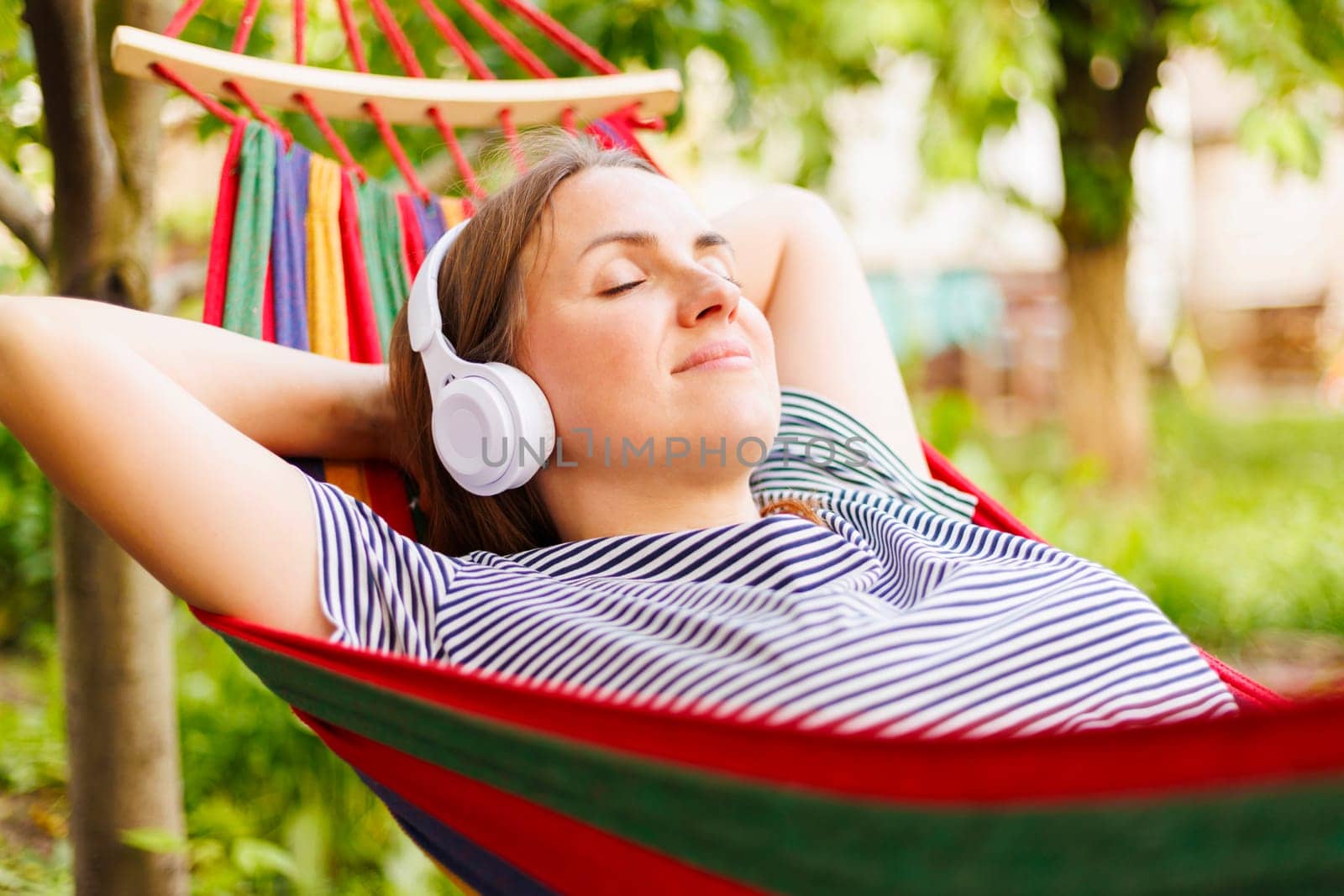 Young woman in headphones listening to music while resting in hammock outdoors.