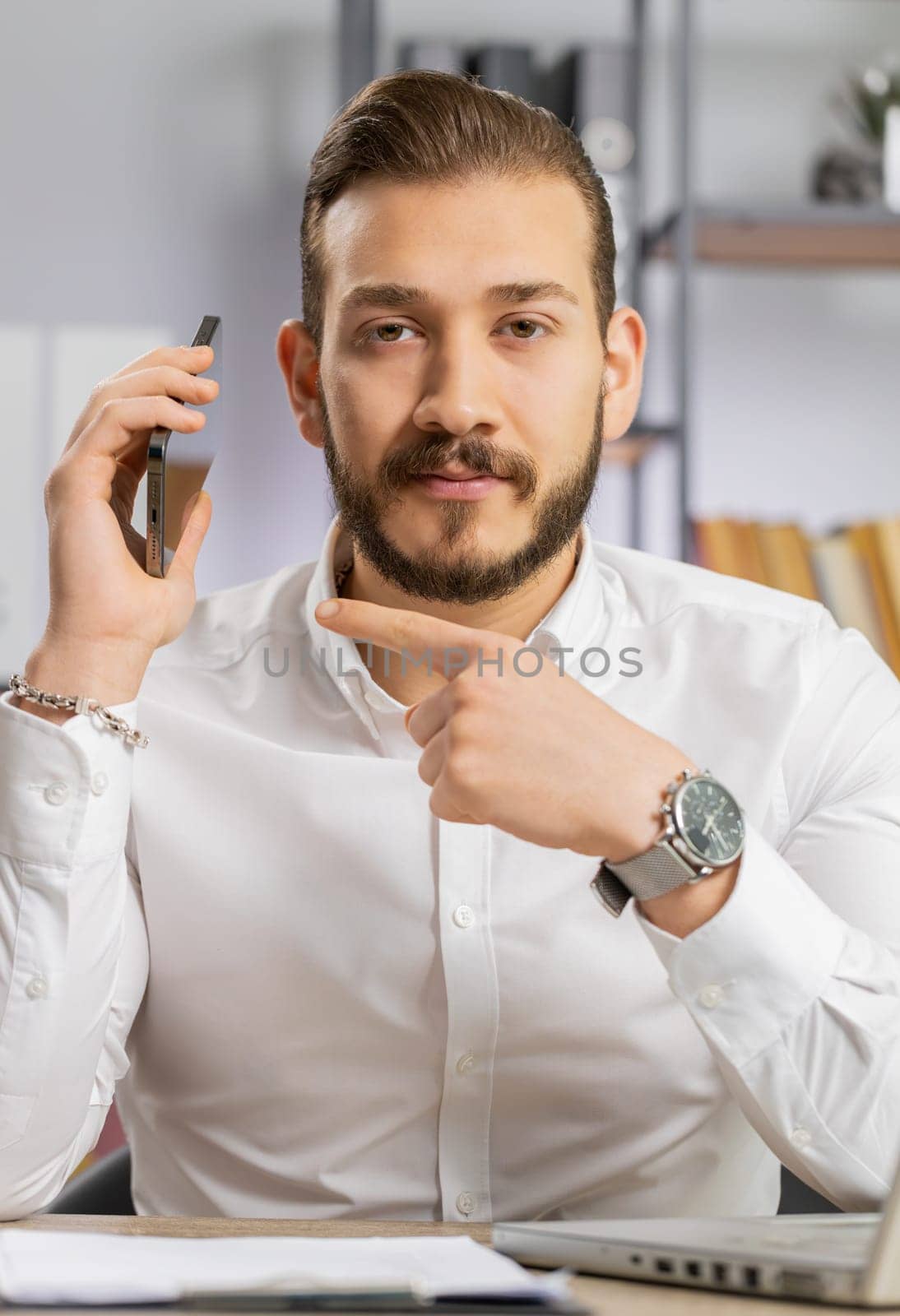 Call me. Middle eastern boss business man showing smartphone asking to make telephone conversation, gesturing call me sign, online date. Freelancer guy at office workplace looking at camera. Vertical