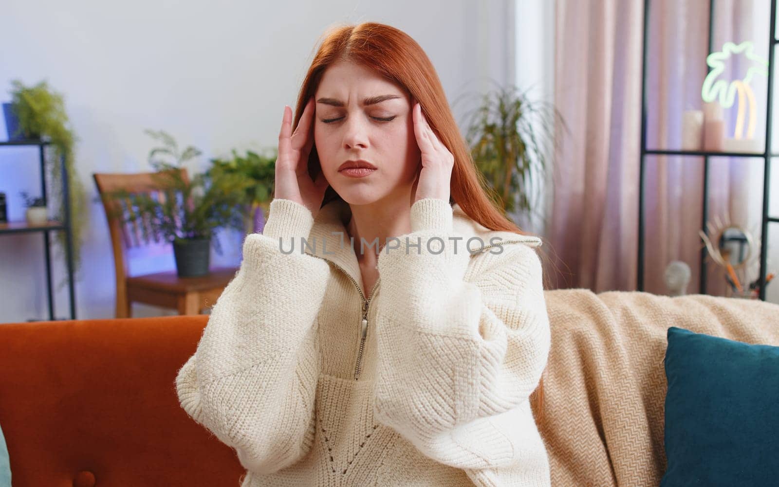 Displeased young woman rubbing temples to cure headache problem, suffering from tension and migraine, stress grimacing in pain high blood pressure at home room apartment. Girl sit on couch. Lifestyles