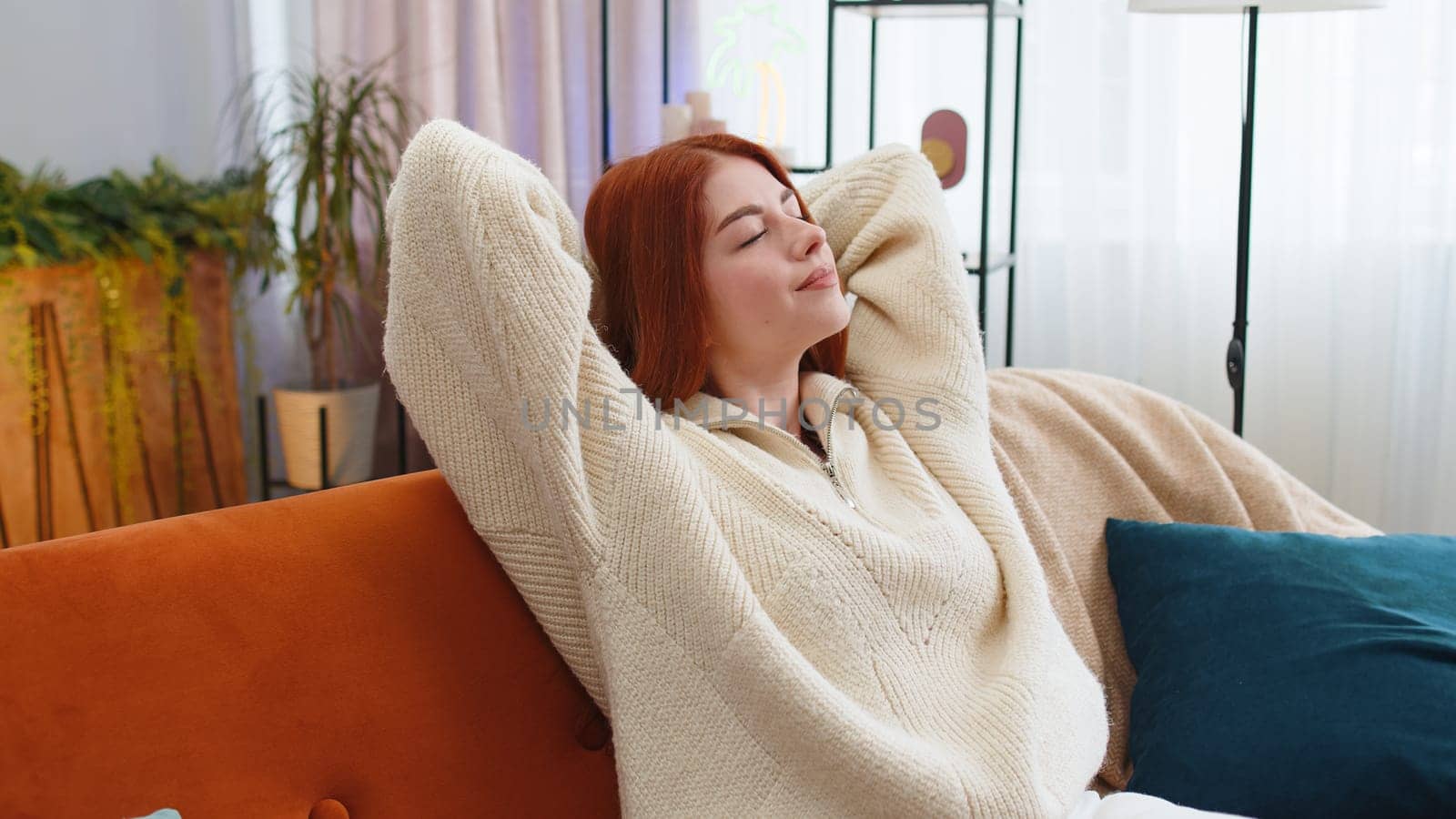 Portrait of tired young woman enjoy relaxing on home couch in room. Happy redhead girl lying on couch resting napping after hard working day, closed her eyes, put hands behind head, stress free, rest