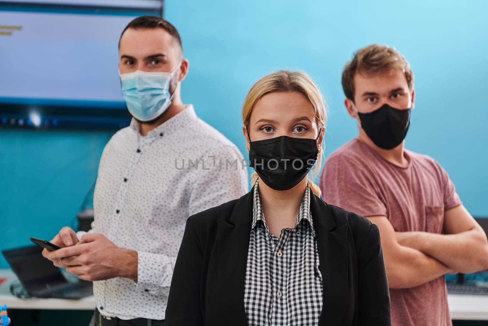 A group of colleagues stand ingin a robotics laboratory, arms crossed, wearing protective masks, symbolizing their teamwork and commitment to technological innovation and scientific research