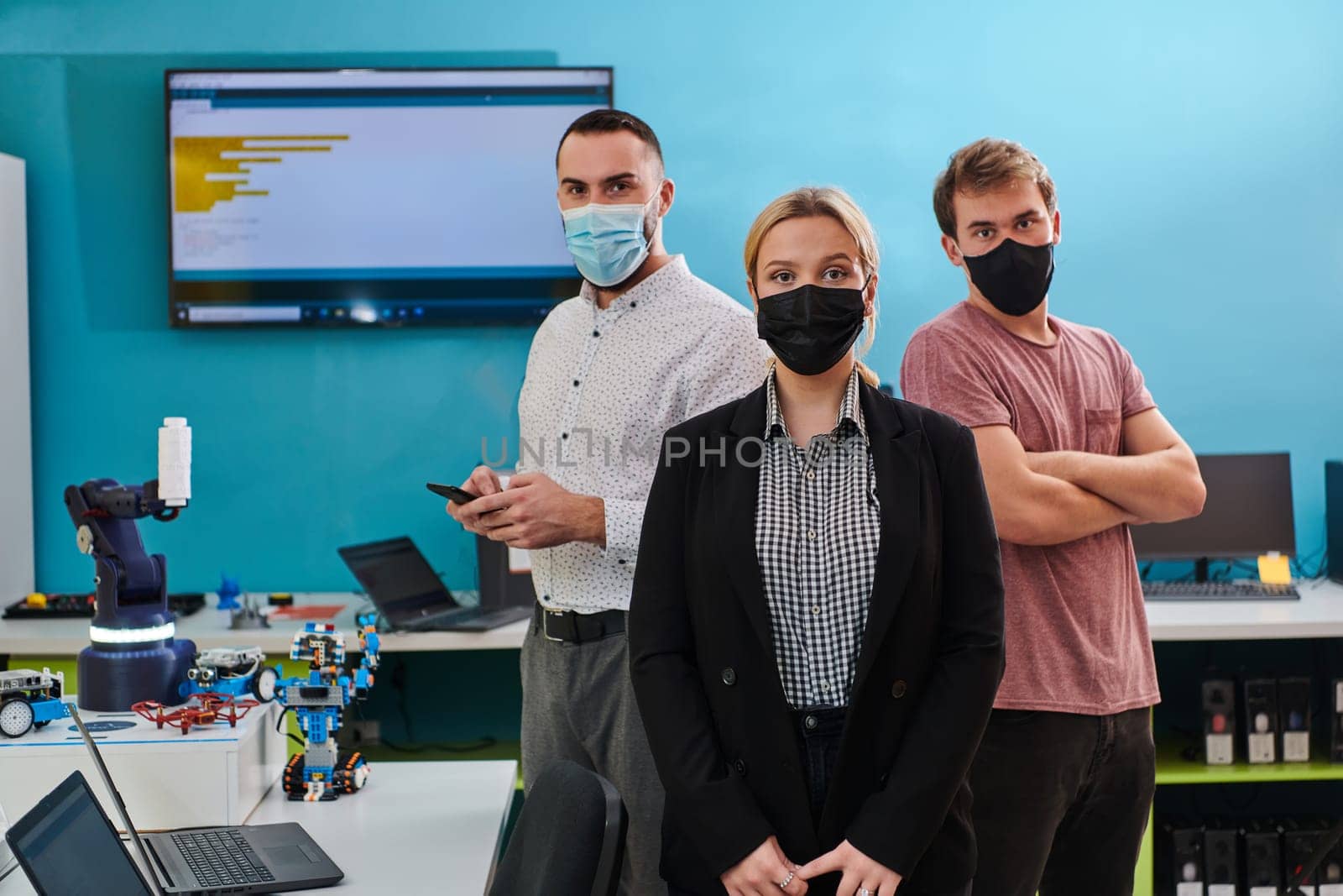 A group of colleagues stand ingin a robotics laboratory, arms crossed, wearing protective masks, symbolizing their teamwork and commitment to technological innovation and scientific research