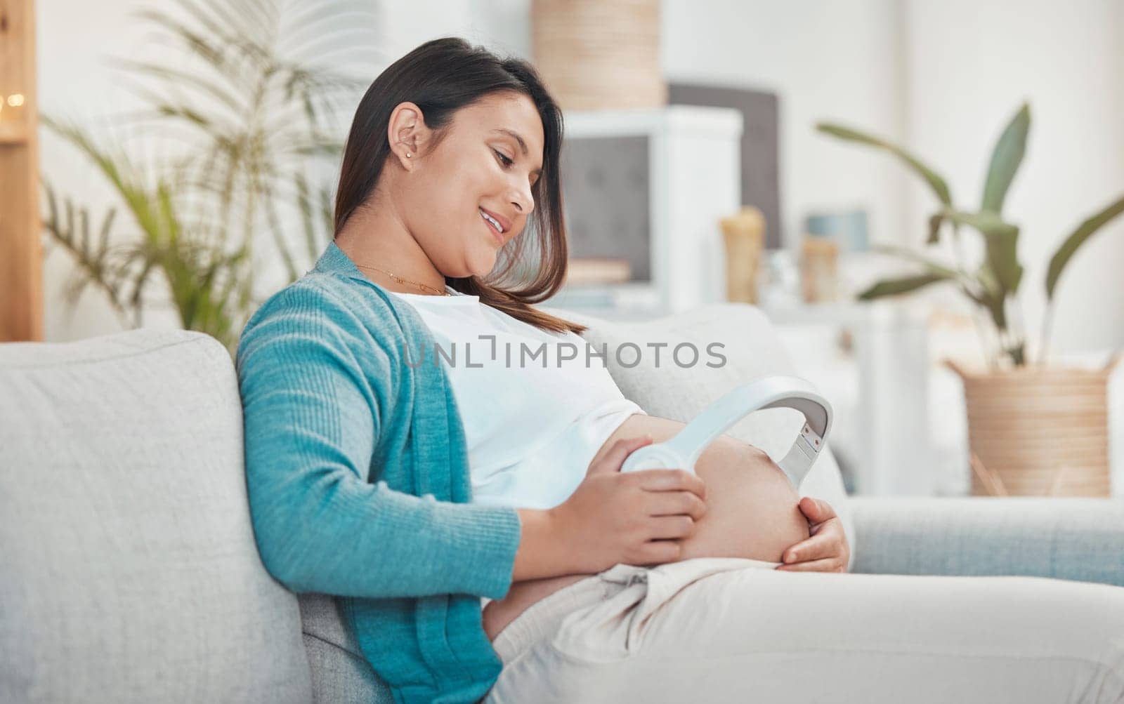 Pregnant, woman and stomach with headphones for music for her unborn baby while relaxing at home. Belly, baby bump and pregnancy with a mother using a headset for audio or podcast streaming by YuriArcurs