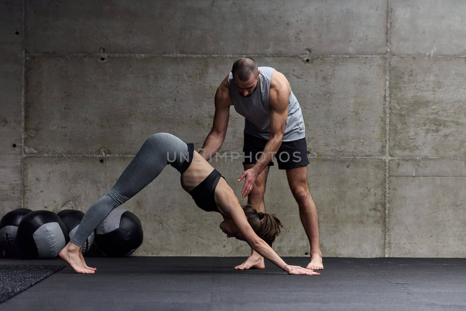 A muscular man assisting a fit woman in a modern gym as they engage in various body exercises and muscle stretches, showcasing their dedication to fitness and benefiting from teamwork and support.