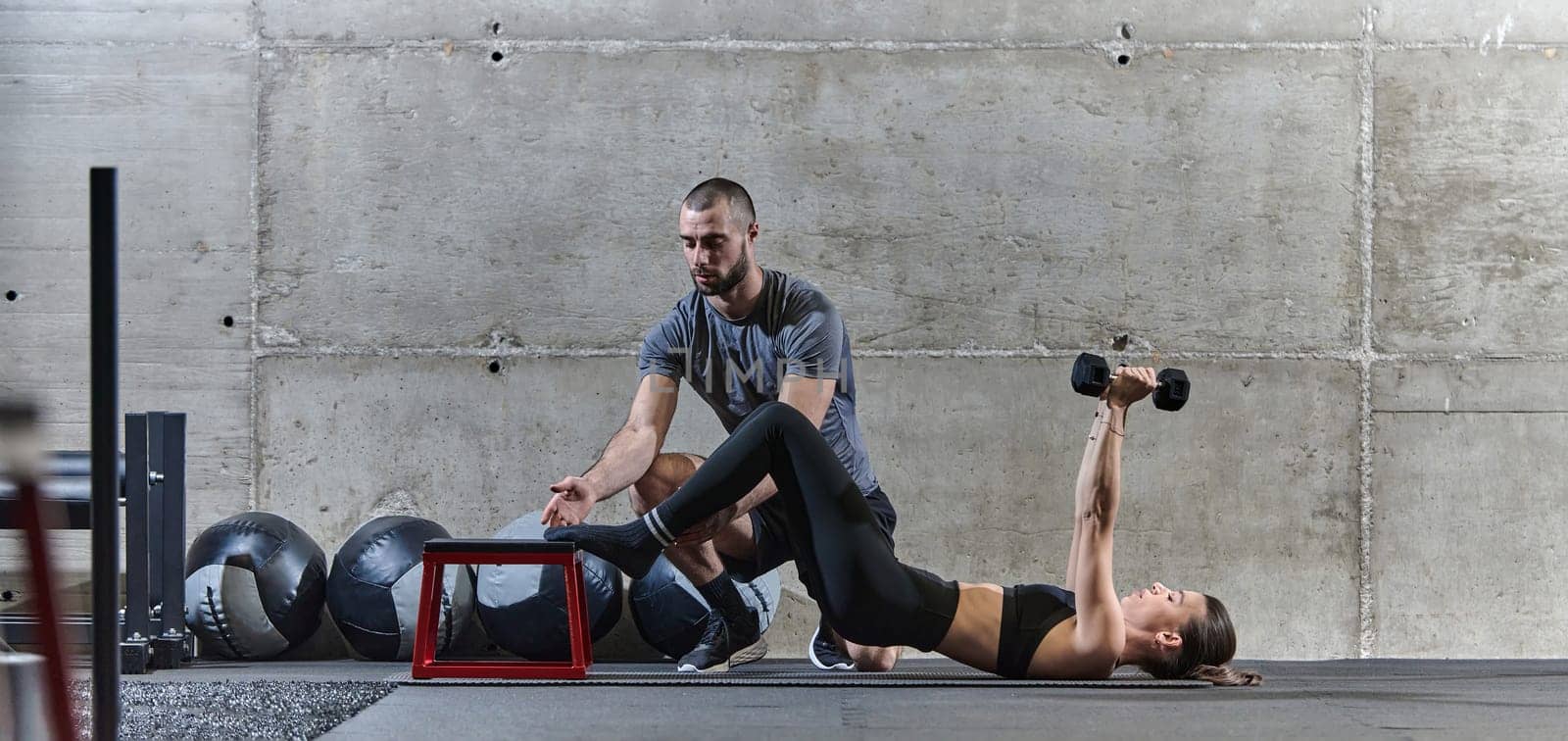 A muscular man assisting a fit woman in a modern gym as they engage in various body exercises and muscle stretches, showcasing their dedication to fitness and benefiting from teamwork and support by dotshock