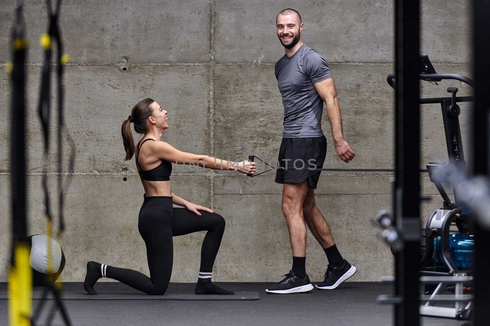 A muscular man assisting a fit woman in a modern gym as they engage in various body exercises and muscle stretches, showcasing their dedication to fitness and benefiting from teamwork and support by dotshock