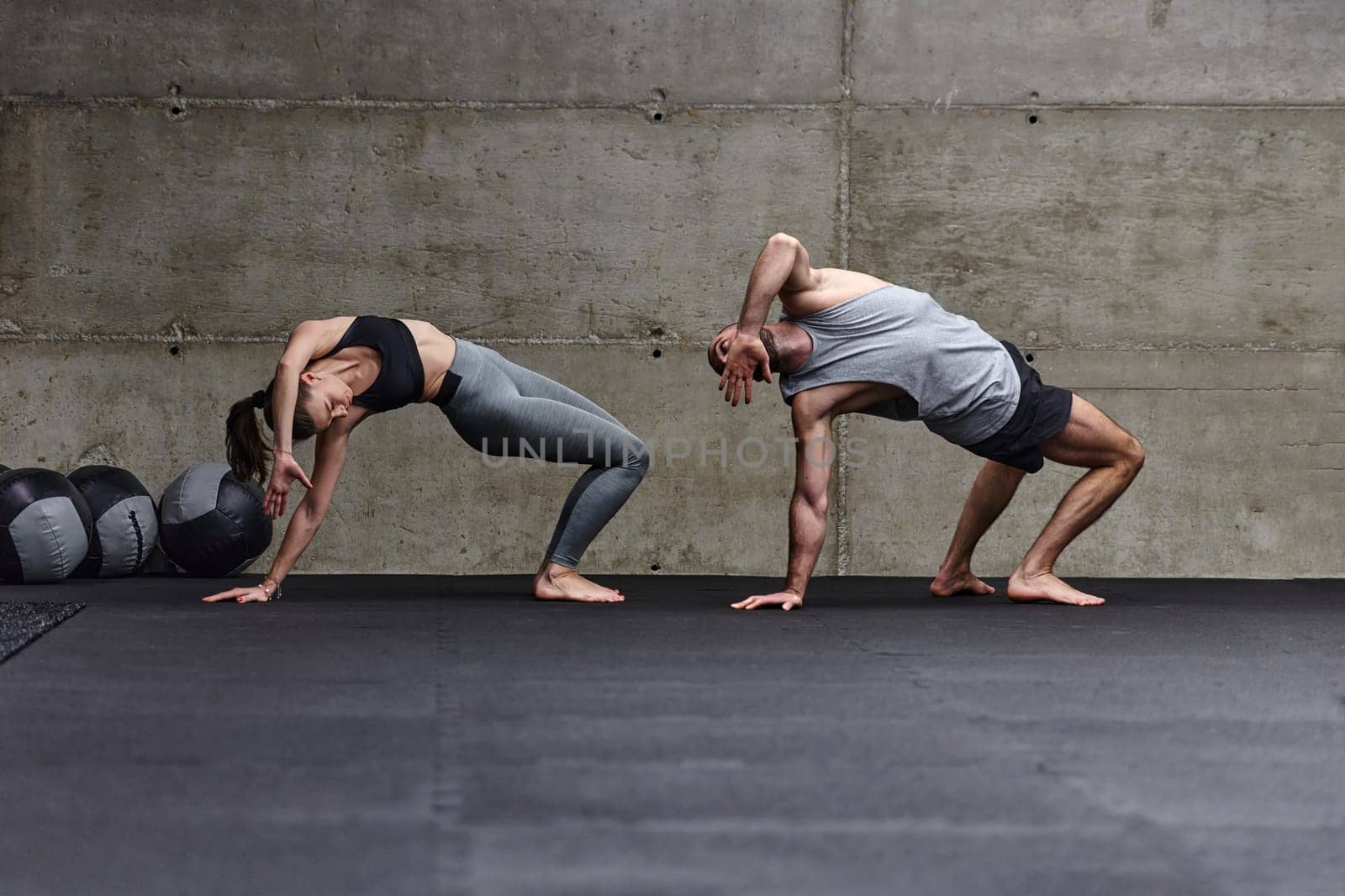 An attractive couple in the gym engaging in various stretching exercises together, showcasing their dedication to fitness, flexibility, and overall wellbeing. With synchronized movements, they demonstrate coordination, balance, and endurance while supporting and motivating each other on their fitness journey.