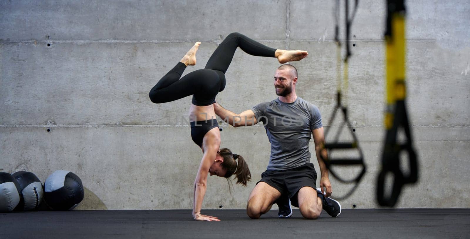 A muscular man assisting a fit woman in a modern gym as they engage in various body exercises and muscle stretches, showcasing their dedication to fitness and benefiting from teamwork and support by dotshock