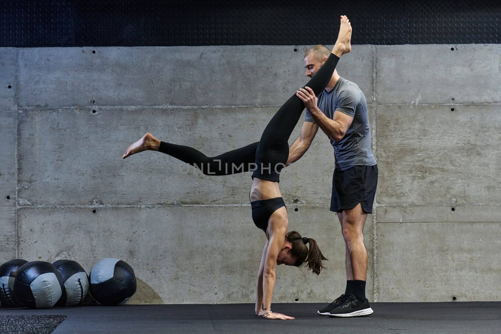 A muscular man assisting a fit woman in a modern gym as they engage in various body exercises and muscle stretches, showcasing their dedication to fitness and benefiting from teamwork and support by dotshock