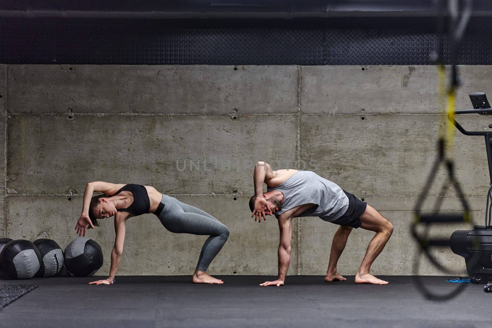 An attractive couple in the gym engaging in various stretching exercises together, showcasing their dedication to fitness, flexibility, and overall wellbeing. With synchronized movements, they demonstrate coordination, balance, and endurance while supporting and motivating each other on their fitness journey.