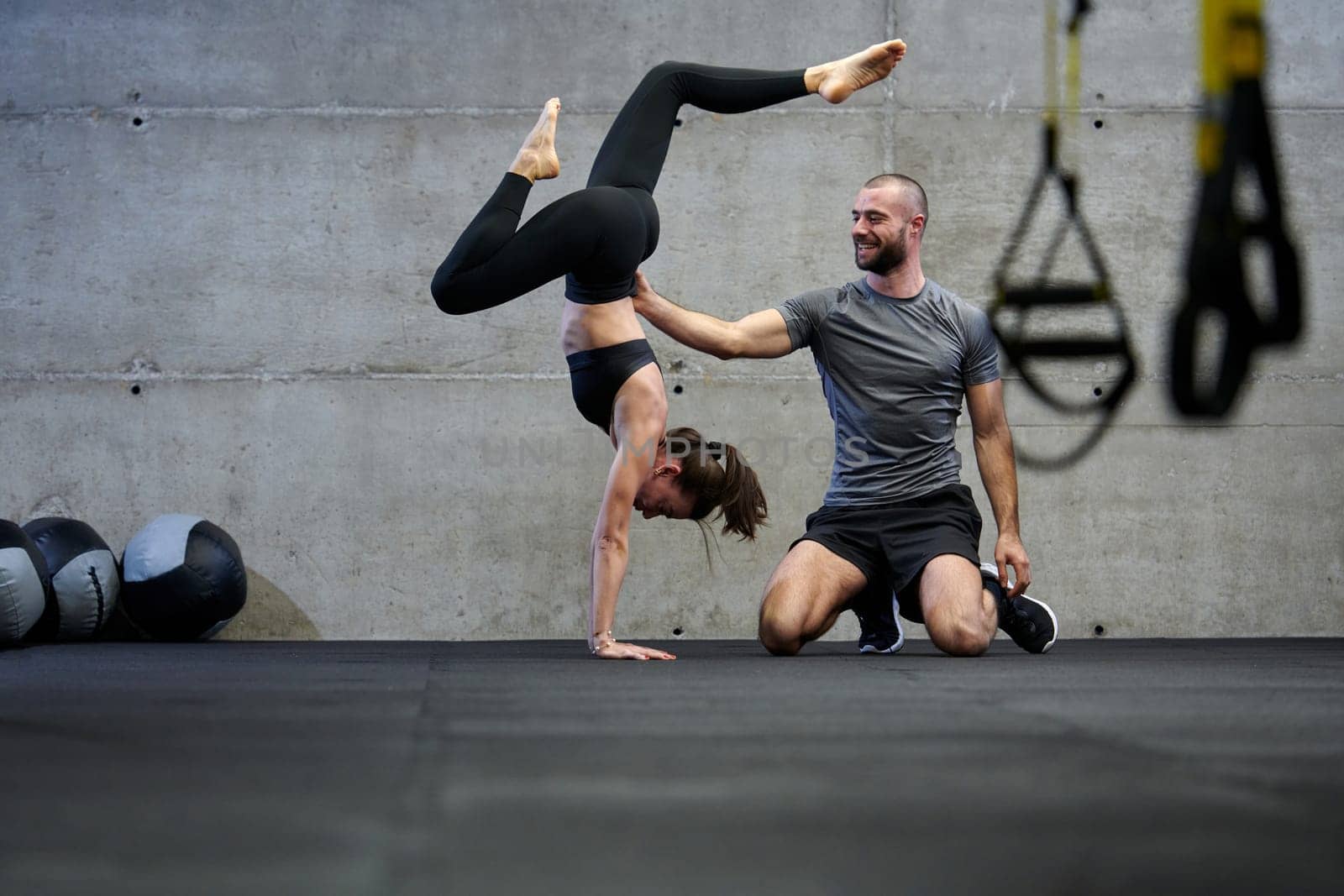 A muscular man assisting a fit woman in a modern gym as they engage in various body exercises and muscle stretches, showcasing their dedication to fitness and benefiting from teamwork and support.