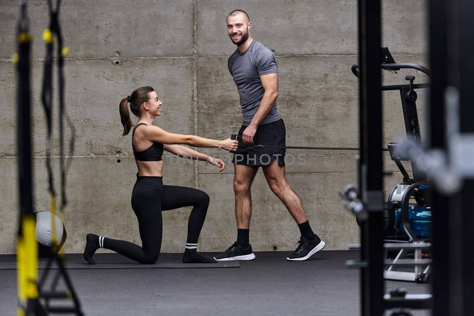 A muscular man assisting a fit woman in a modern gym as they engage in various body exercises and muscle stretches, showcasing their dedication to fitness and benefiting from teamwork and support by dotshock