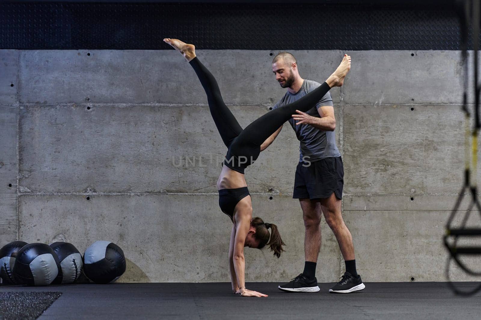 A muscular man assisting a fit woman in a modern gym as they engage in various body exercises and muscle stretches, showcasing their dedication to fitness and benefiting from teamwork and support by dotshock