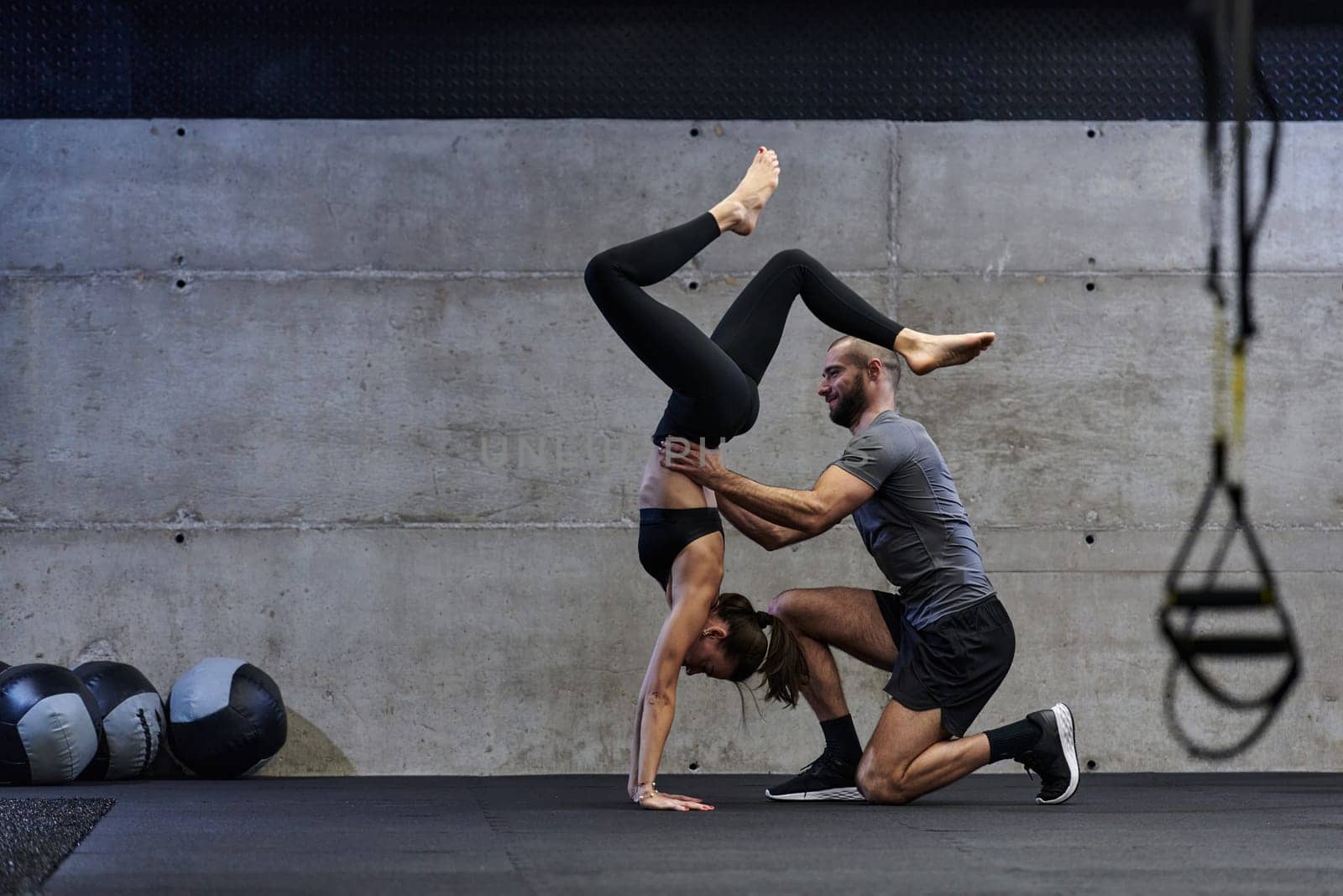 A muscular man assisting a fit woman in a modern gym as they engage in various body exercises and muscle stretches, showcasing their dedication to fitness and benefiting from teamwork and support.