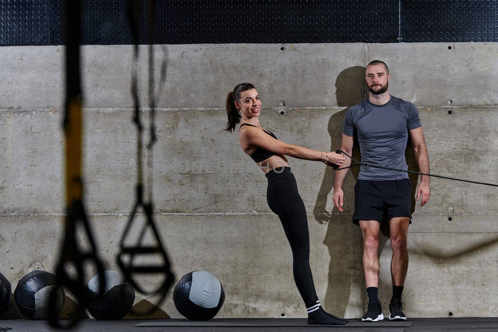 A muscular man assisting a fit woman in a modern gym as they engage in various body exercises and muscle stretches, showcasing their dedication to fitness and benefiting from teamwork and support by dotshock