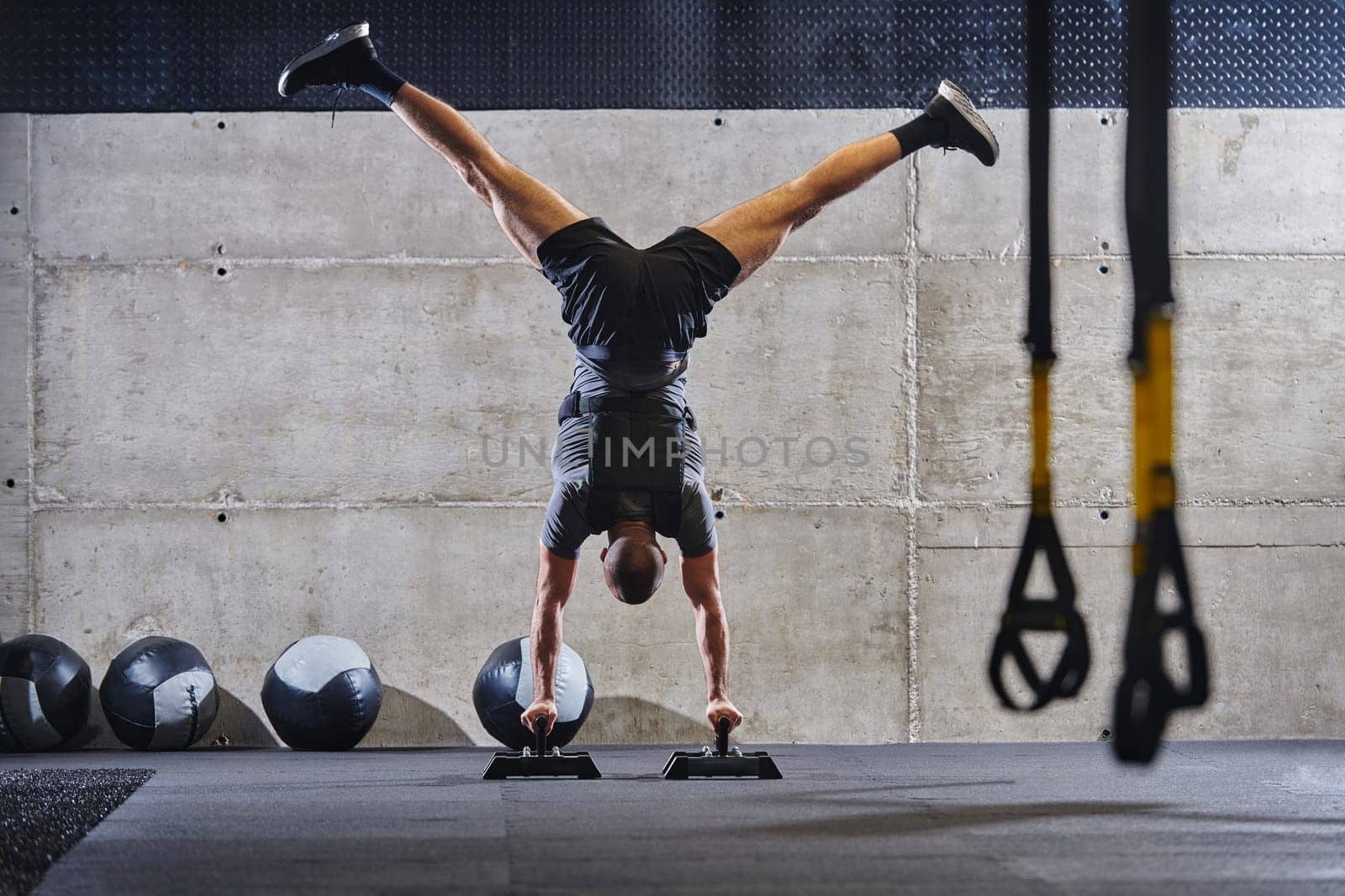 A muscular man in a handstand position, showcasing his exceptional balance and body control while performing a variety of exercises to enhance his overall body stability and strength in a modern gym.