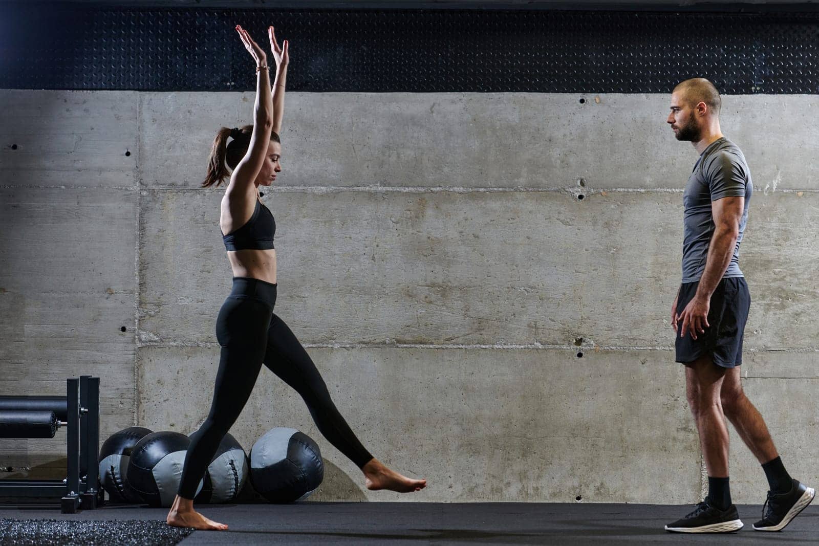 A muscular man assisting a fit woman in a modern gym as they engage in various body exercises and muscle stretches, showcasing their dedication to fitness and benefiting from teamwork and support by dotshock