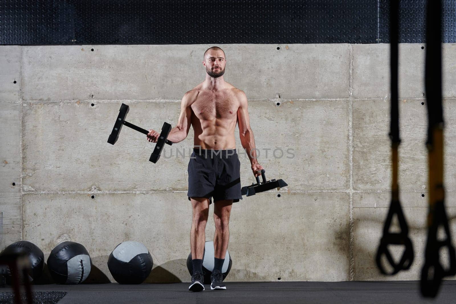 A muscular man performs shoulder exercises in a modern gym, showcasing his strength and dedication to fitness