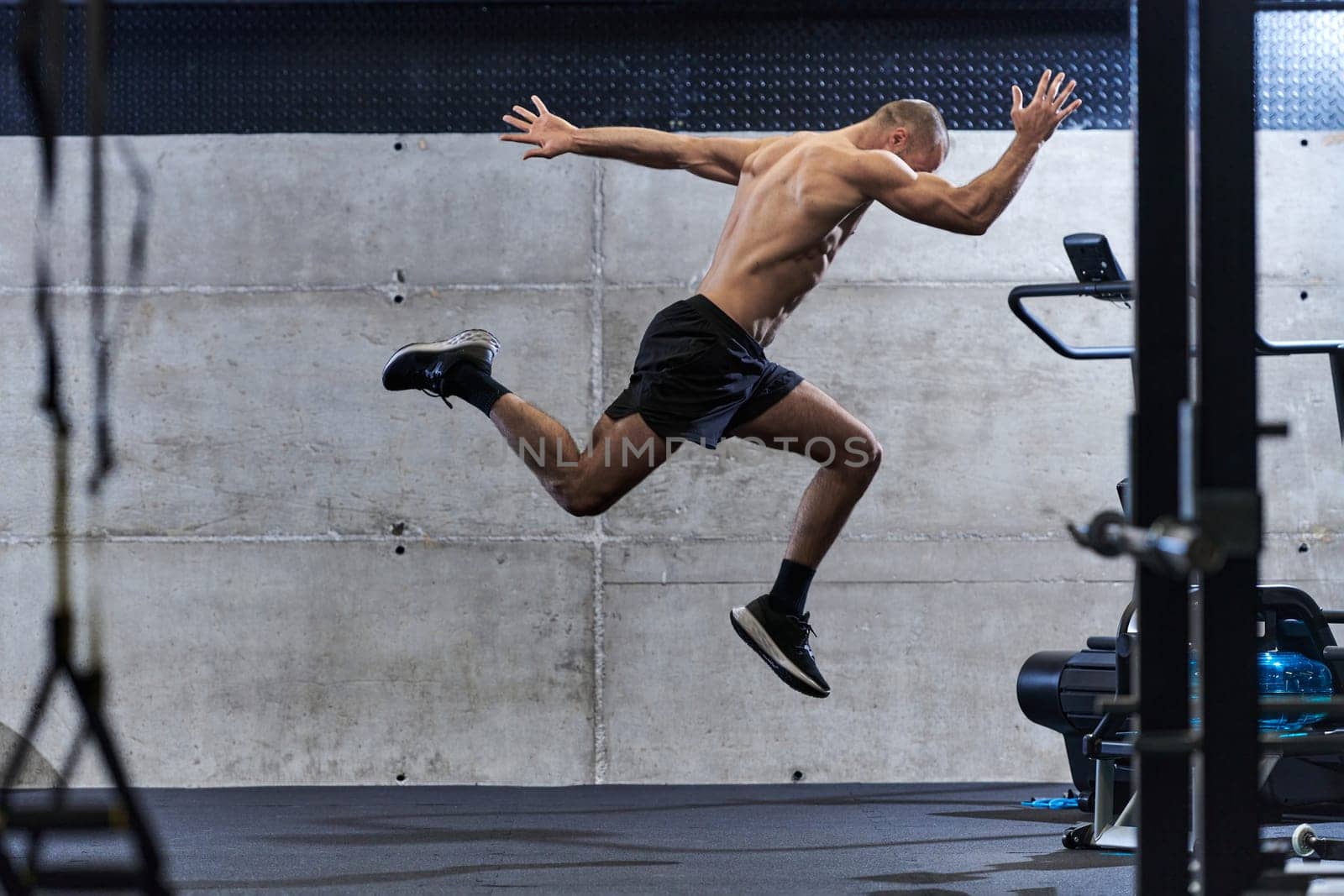 A muscular man captured in air as he jumps in a modern gym, showcasing his athleticism, power, and determination through a highintensity fitness routine.