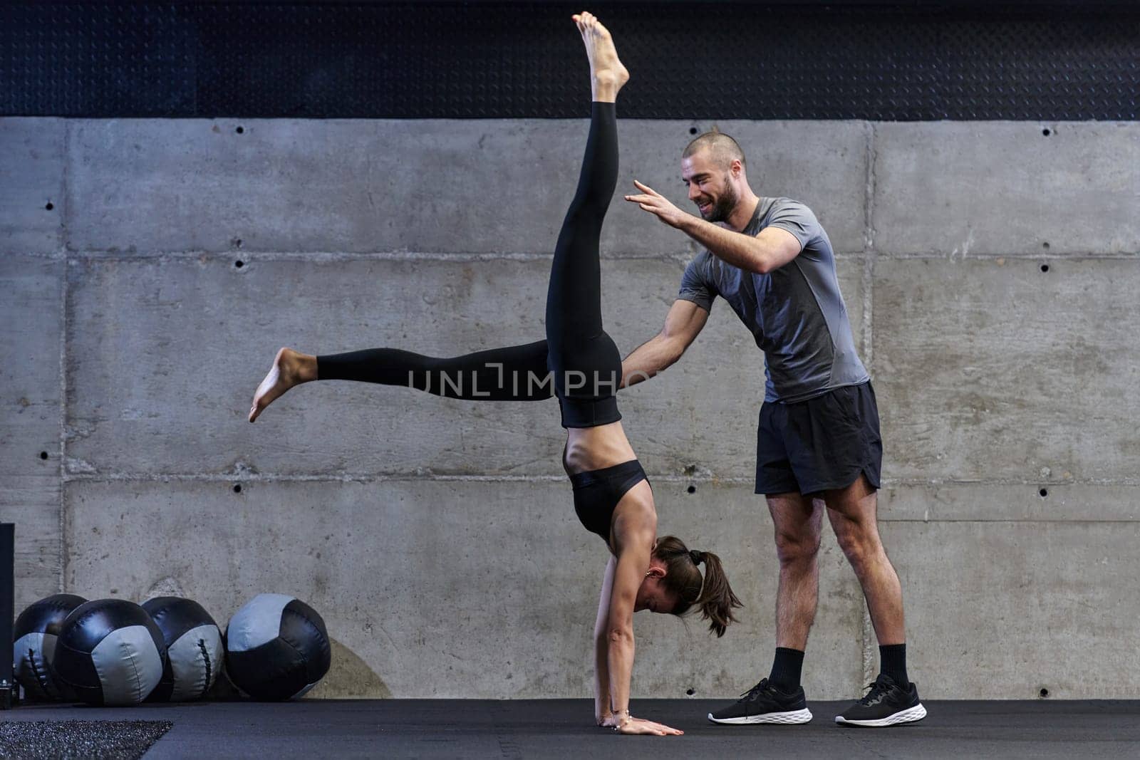 A muscular man assisting a fit woman in a modern gym as they engage in various body exercises and muscle stretches, showcasing their dedication to fitness and benefiting from teamwork and support.