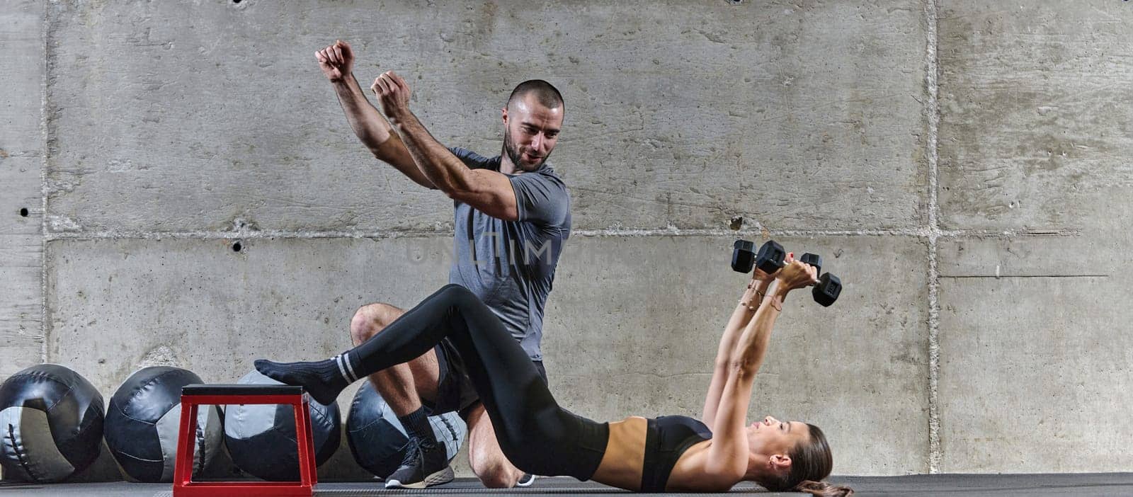 A muscular man assisting a fit woman in a modern gym as they engage in various body exercises and muscle stretches, showcasing their dedication to fitness and benefiting from teamwork and support.