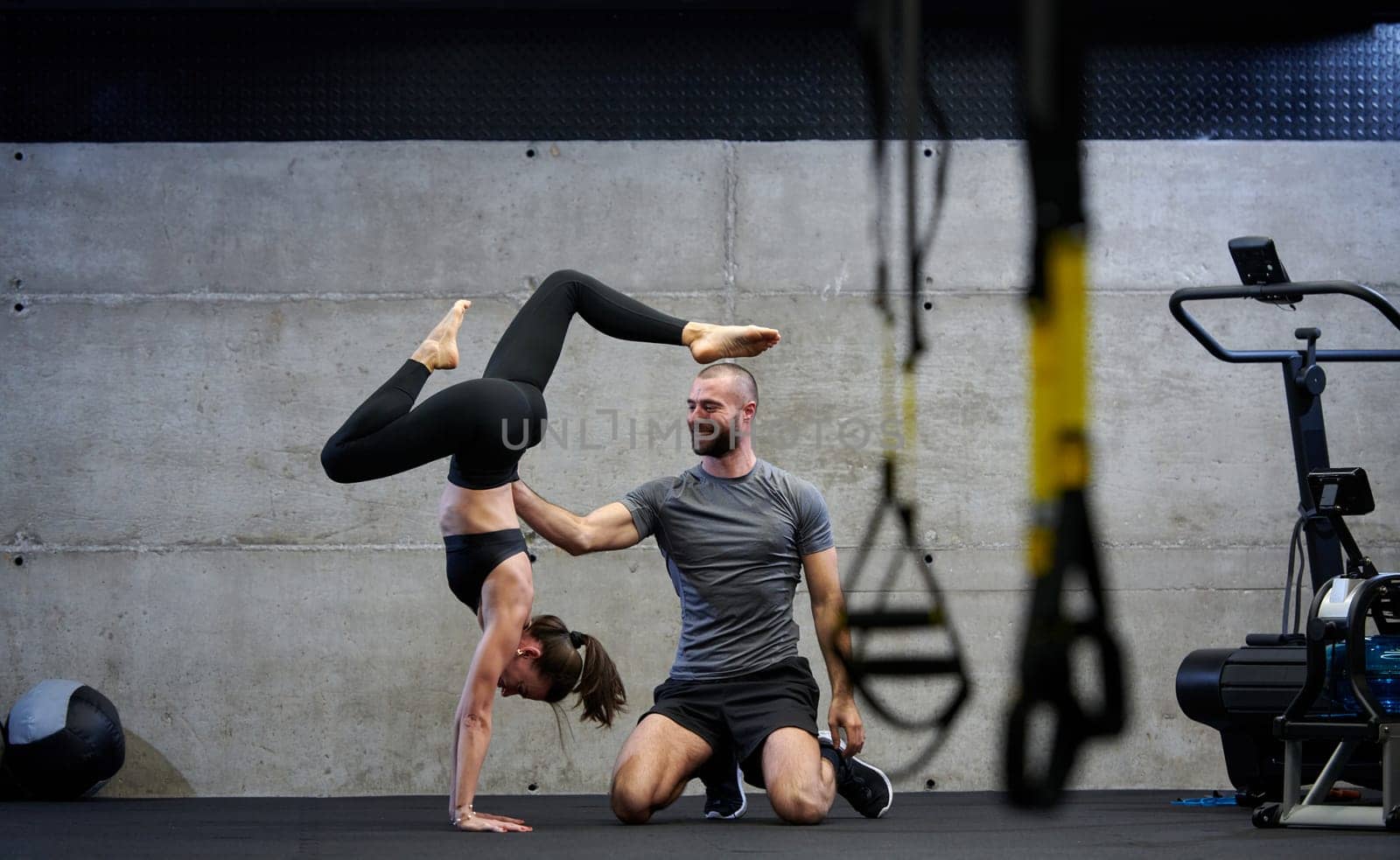 A muscular man assisting a fit woman in a modern gym as they engage in various body exercises and muscle stretches, showcasing their dedication to fitness and benefiting from teamwork and support by dotshock