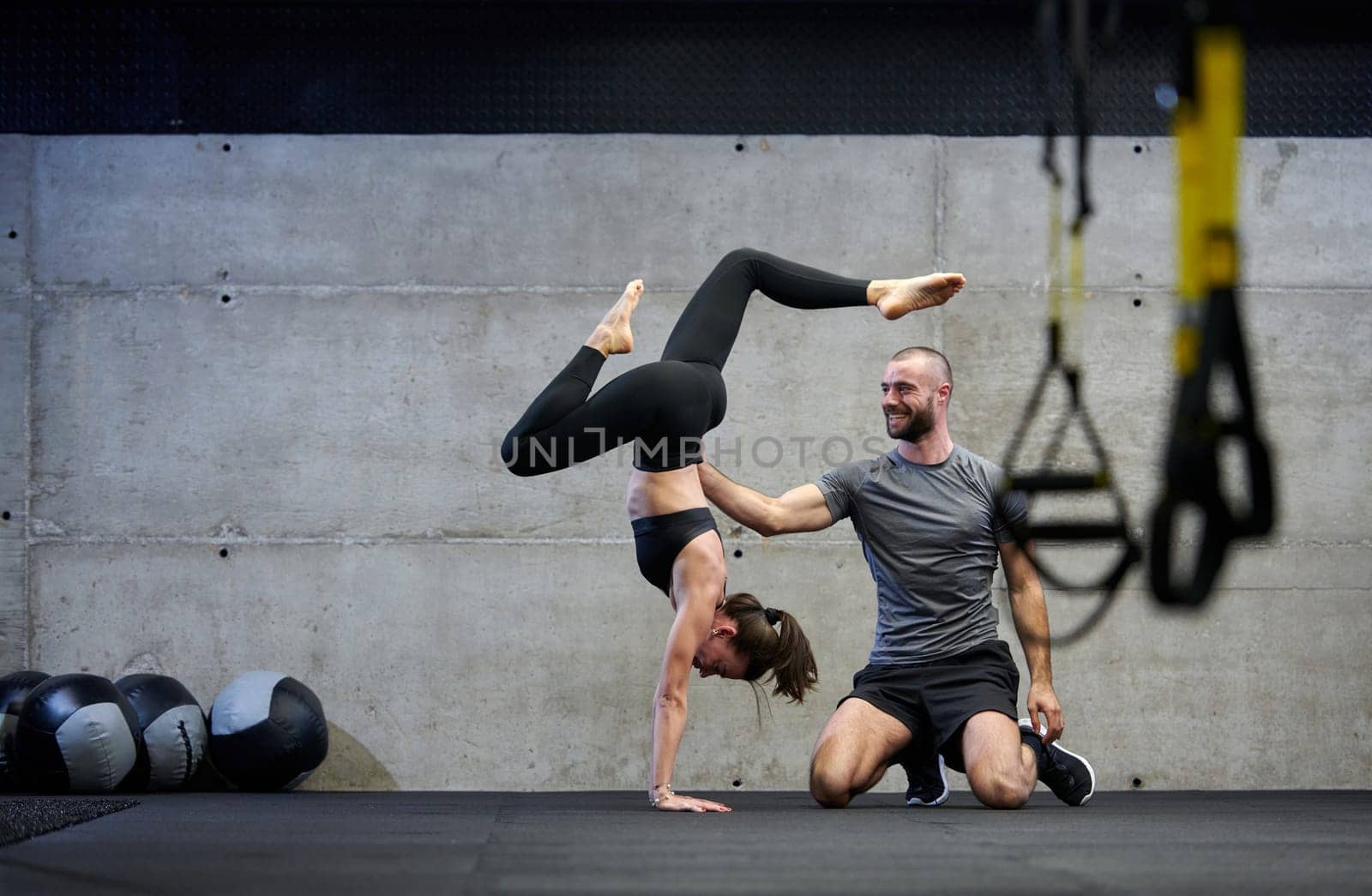 A muscular man assisting a fit woman in a modern gym as they engage in various body exercises and muscle stretches, showcasing their dedication to fitness and benefiting from teamwork and support.