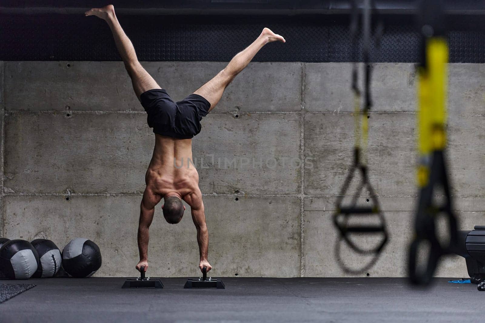 A muscular man in a handstand position, showcasing his exceptional balance and body control while performing a variety of exercises to enhance his overall body stability and strength in a modern gym.