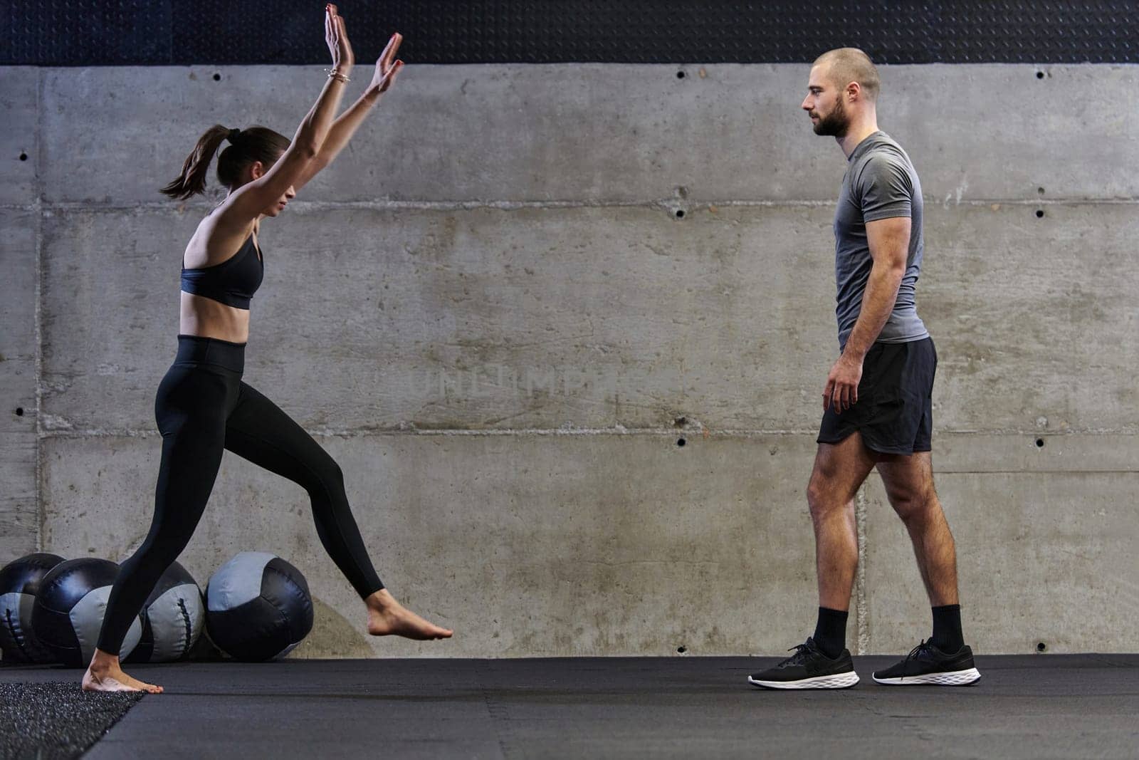 A muscular man assisting a fit woman in a modern gym as they engage in various body exercises and muscle stretches, showcasing their dedication to fitness and benefiting from teamwork and support by dotshock