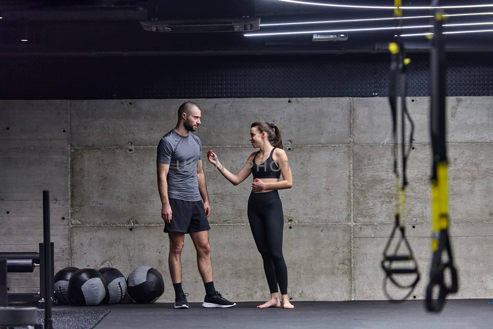 Muscular man and fit woman in a conversation before commencing their training session in a modern gym. by dotshock