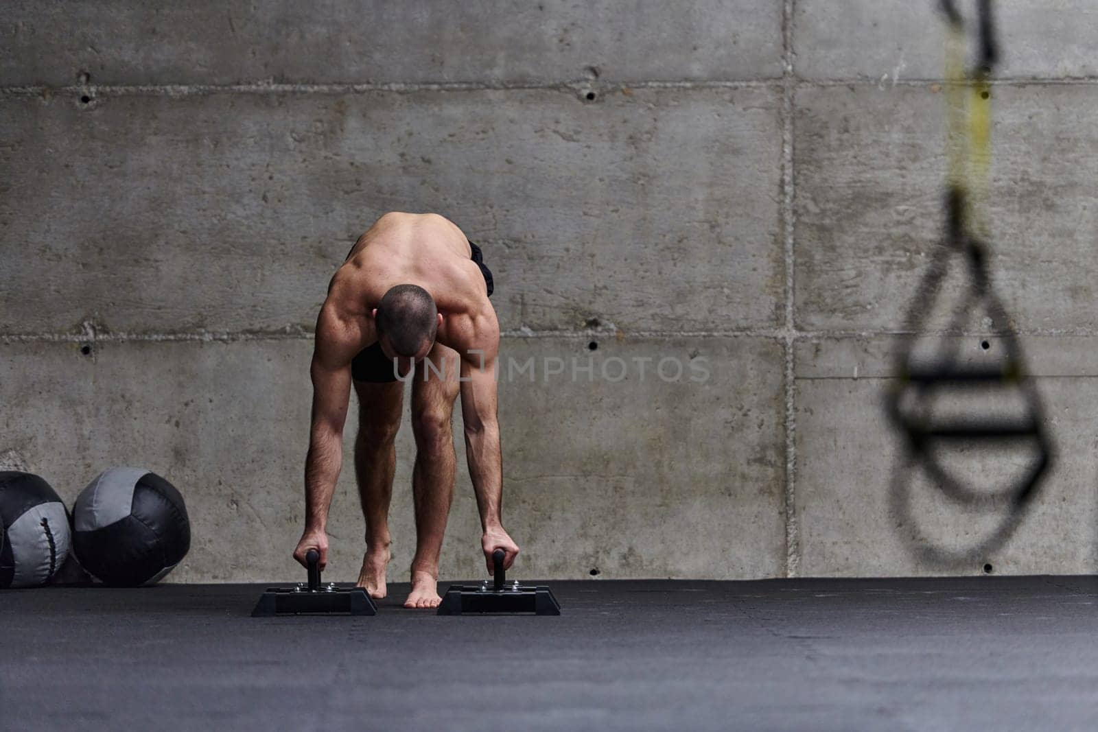 A muscular man in a handstand position, showcasing his exceptional balance and body control while performing a variety of exercises to enhance his overall body stability and strength in a modern gym.