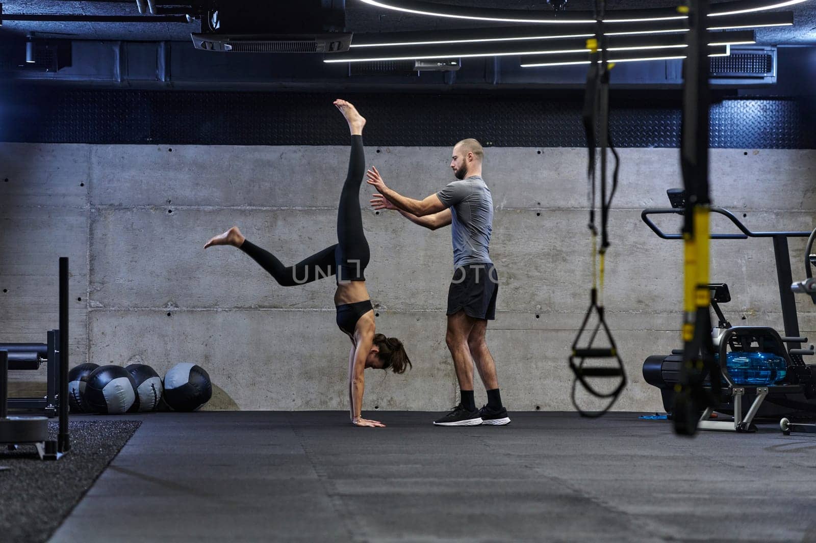 A muscular man assisting a fit woman in a modern gym as they engage in various body exercises and muscle stretches, showcasing their dedication to fitness and benefiting from teamwork and support by dotshock