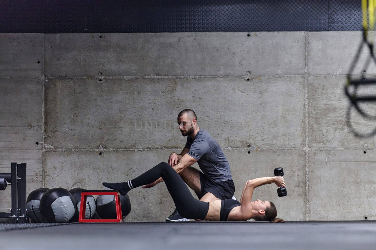 A muscular man assisting a fit woman in a modern gym as they engage in various body exercises and muscle stretches, showcasing their dedication to fitness and benefiting from teamwork and support by dotshock