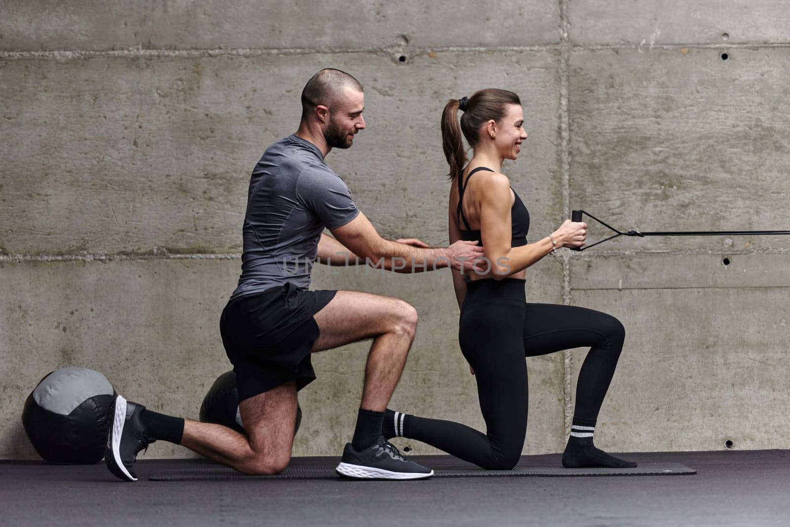 A muscular man assisting a fit woman in a modern gym as they engage in various body exercises and muscle stretches, showcasing their dedication to fitness and benefiting from teamwork and support.