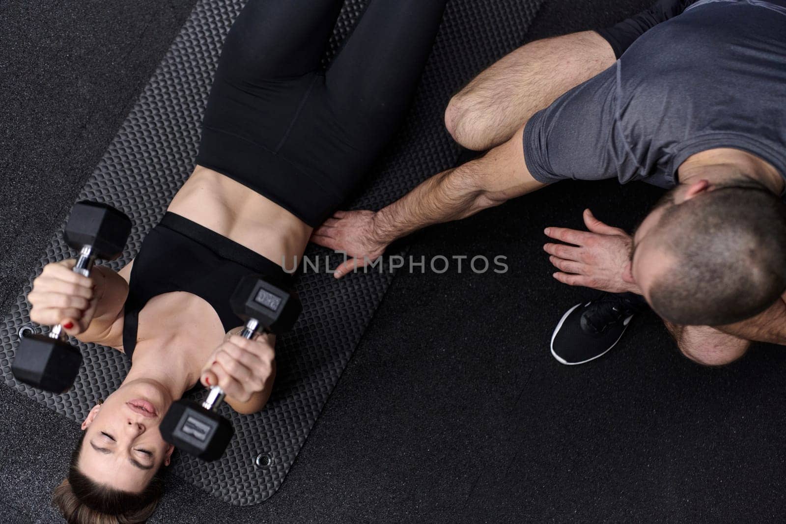 A muscular man assisting a fit woman in a modern gym as they engage in various body exercises and muscle stretches, showcasing their dedication to fitness and benefiting from teamwork and support by dotshock