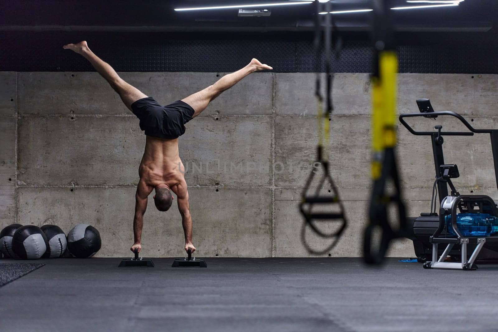 A muscular man in a handstand position, showcasing his exceptional balance and body control while performing a variety of exercises to enhance his overall body stability and strength in a modern gym.