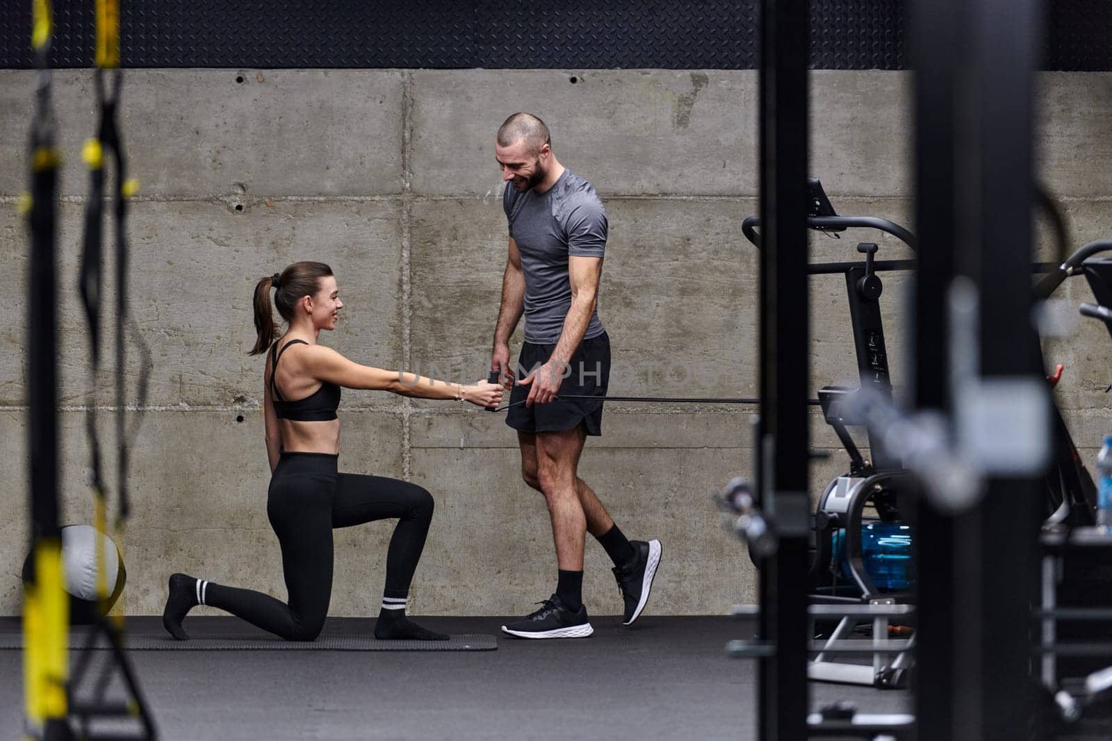 A muscular man assisting a fit woman in a modern gym as they engage in various body exercises and muscle stretches, showcasing their dedication to fitness and benefiting from teamwork and support by dotshock