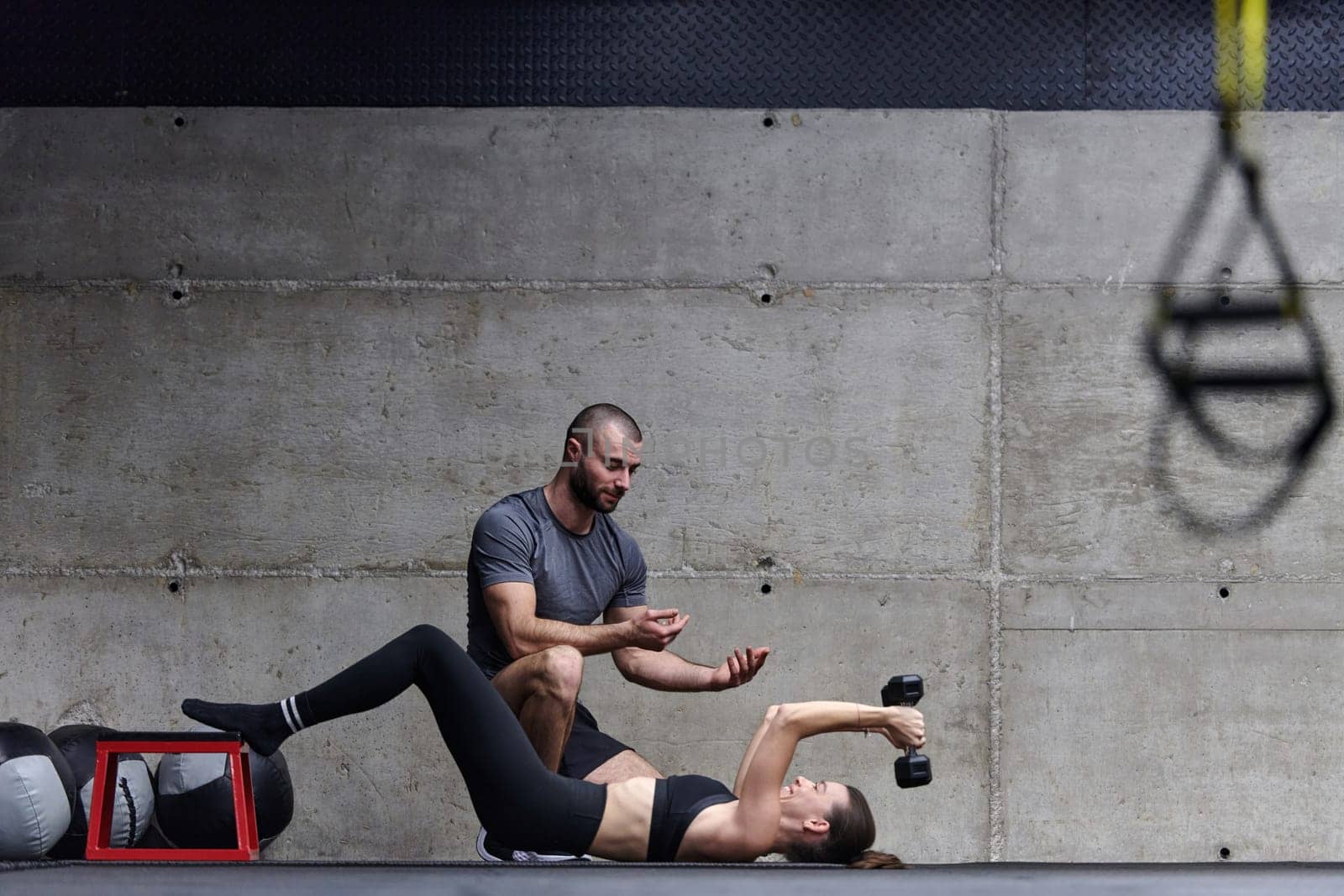 A muscular man assisting a fit woman in a modern gym as they engage in various body exercises and muscle stretches, showcasing their dedication to fitness and benefiting from teamwork and support by dotshock