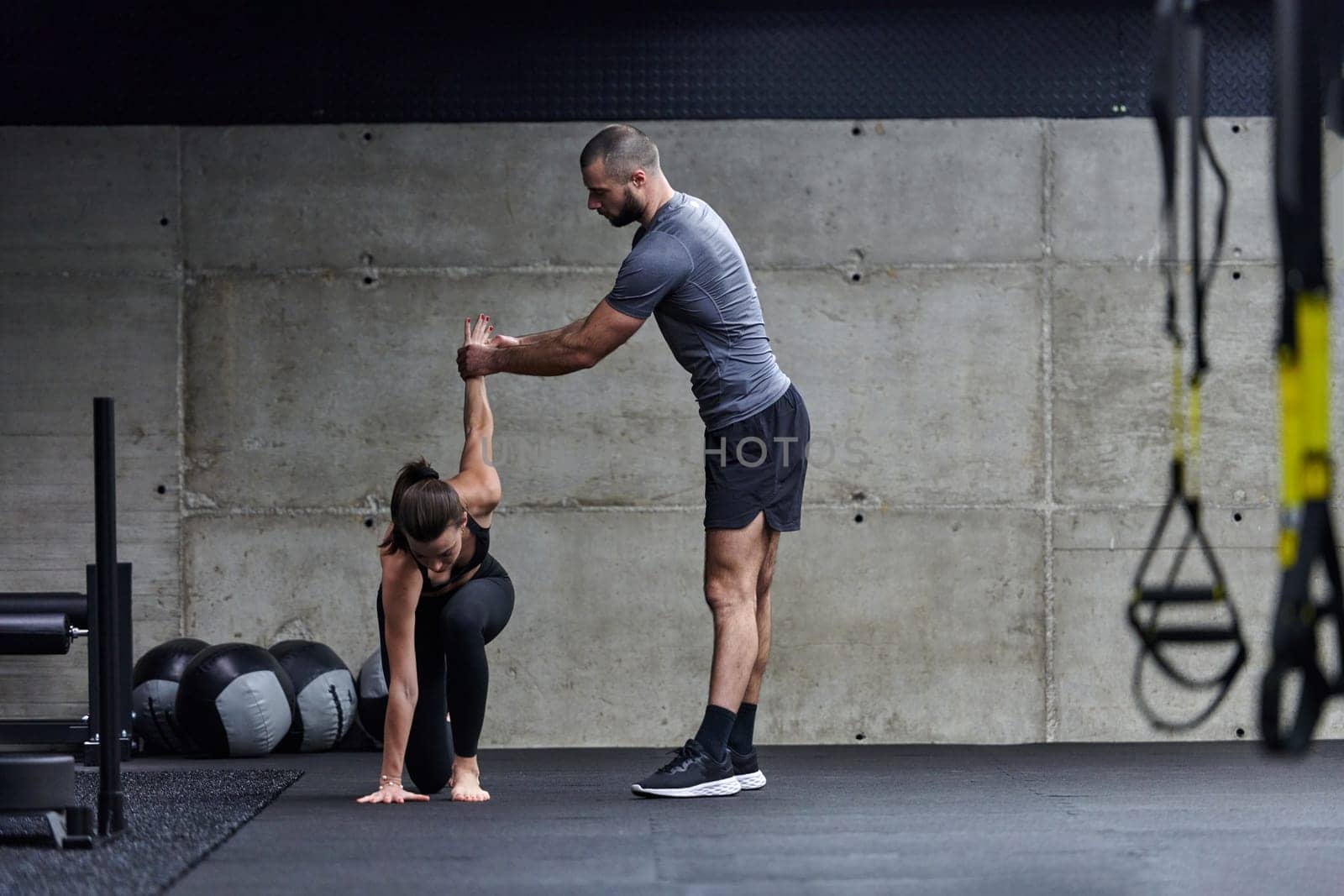 A muscular man assisting a fit woman in a modern gym as they engage in various body exercises and muscle stretches, showcasing their dedication to fitness and benefiting from teamwork and support by dotshock