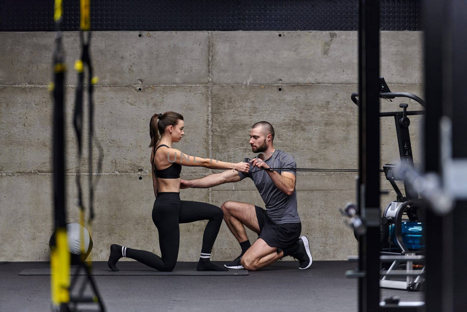 A muscular man assisting a fit woman in a modern gym as they engage in various body exercises and muscle stretches, showcasing their dedication to fitness and benefiting from teamwork and support.