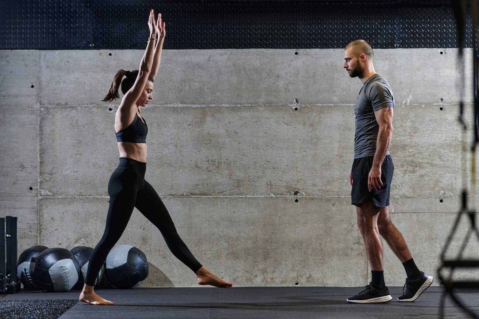 A muscular man assisting a fit woman in a modern gym as they engage in various body exercises and muscle stretches, showcasing their dedication to fitness and benefiting from teamwork and support by dotshock